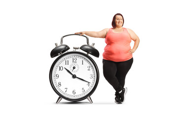 Corpulent woman in sportswear leaning on a big alarm clock
