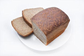 A black loaf of bread cut on a white plate. Slices of bread. Breakfast from a bun.