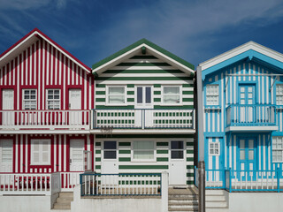 Nice typical houses with colorful stripes in Costa Nova, Aveiro, Portugal. Sunny day on a summer day. Contrasts of colors white, red, green and blue. Travel concept.
