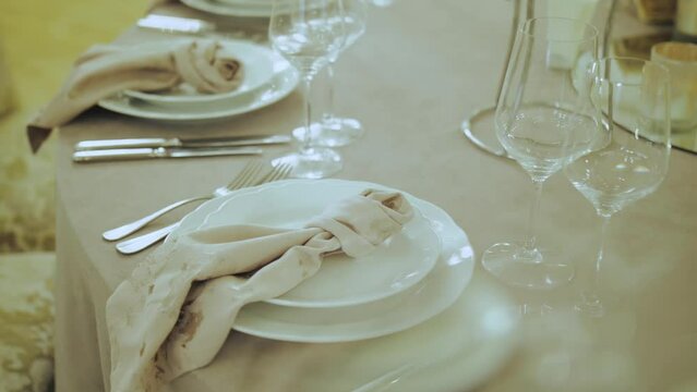Close-up wedding table decoration served plates with napking, glasses on the table. Beautiful wedding table decor, all decorated in pastel colors, camera moving slow motion. 