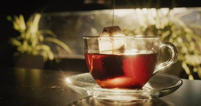 A tea bag is dipped into a cup of boiling water. The sun shines beautifully from the window - the beginning of a good day concept