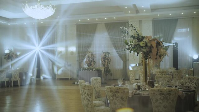 Wedding tables decoration with big floral composition, served plates and glasses. Light rays through the banquet hall. All decorated in pastel colors, camera moving slow motion. 