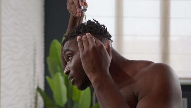 African American man applying argan oil serum on hair roots dreadlocks healthy massage morning bathroom routine male guy drip keratin cosmetic liquid treatment baldness alopecia beauty care for hairdo