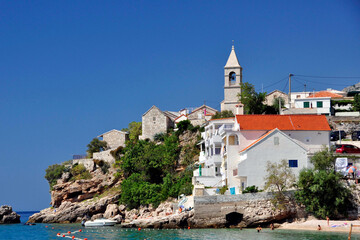 Mały półwysep w miejscowości Pisak, ze ścisłą zabudową na skalnym wybrzeżu, nad którą góruje kościół, na tle błękitnego nieba. Chorwacja. 