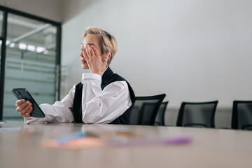 Low-angle view of tired middle-aged businesswoman using mobile phone at office desk, feeling...