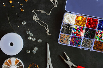 Box with colorful beads, string, wire, chain, scissors, pliers and hammer on dark background. Various jewelry making supplies. Top view. - obrazy, fototapety, plakaty