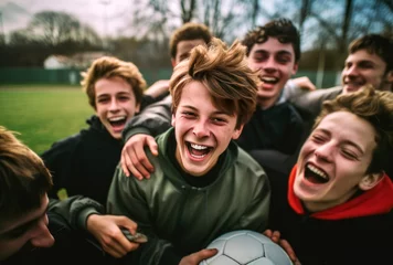 Fotobehang A high school soccer team of teenage boys revels in the excitement of their recent victory. Gathered on the field, their faces glowing, they personify the essence of friendship and teamwork in sports. © InputUX