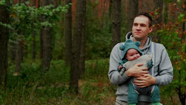 Young father with his newborn baby in a sling walking in the autumn forest. The concept of a happy family.