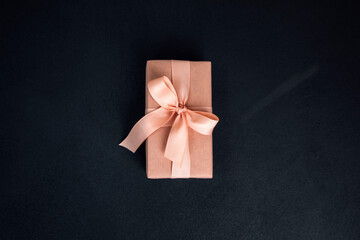 Background for greetings. Gifts wrapping in soft pink paper with pink ribbon on a black concrete...