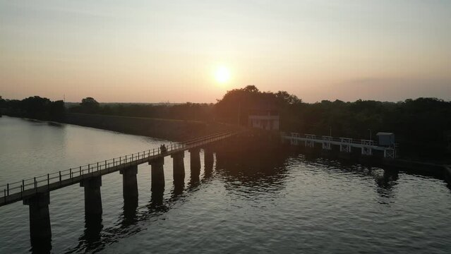 Aerial footage of a bike passing on a bridge built in the midst of a lake during the rural evening sunset, capturing rural life.
