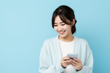 Fototapeta premium Cute Japenese Fictional Woman Using Phone and Smiling. Isolated on a Plain Light Blue Background. Generative AI.