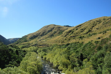 Scenic view of a river flowing through hills covered with shrubs against a lake in Otago,New Zealand