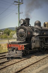 Fototapeta na wymiar Aged, corroded train engine travels along a track in a train yard with a plume of smoke