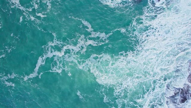 Aerial view of tranquil foam waves breaking rocky cliff in a daytime