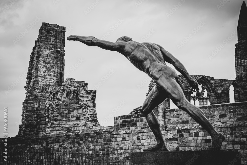 Sticker Grayscale shot of the Whitby Gladiator statue with ruins of Whitby Abbey in North Yorkshire, England