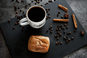 A cup of coffee, a bun and cinnamon with star anise on a gray background