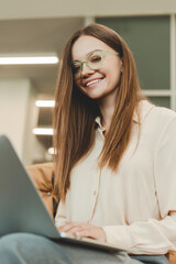 Beautiful smiling young woman wearing eyeglasses, using laptop, working online, checking mail