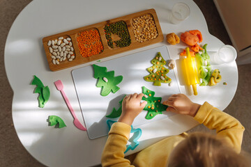 Naklejka na ściany i meble Child hands creating Christmas tree from play dough for modeling with decorate from dried beans. Holiday Art Activity for Kids. Fine motor skills. Sensory play for toddlers.