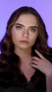 young woman with curly shiny hairstyle and smokey eyes make-up posing on color background