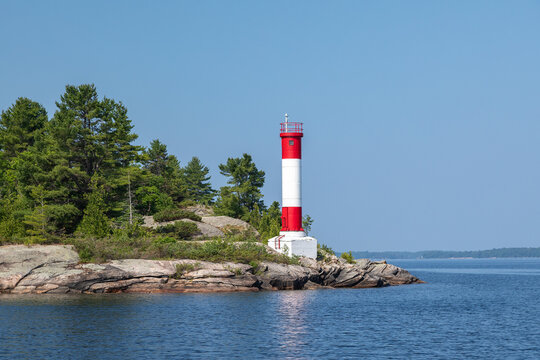 A Red and White Lighthouse on a Rocky Point of Land on Clear Blue Sky Summer Day in Parry Sound, Lake Huron, Georgian Bay, Ontario, Canada