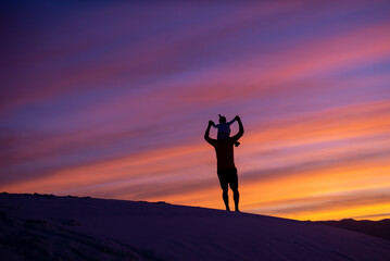 Father & daughter silhouette sitting on shoulders with purple sunset at White Sands National Park