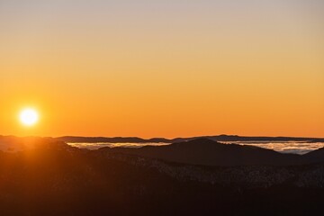 the sun setting on a mountain with clouds in the foreground