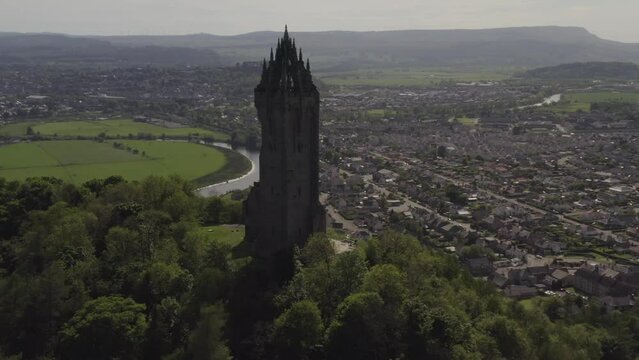 Aerial flying around National Wallace Monument landmark on hill with Stirling city, river, scottish highlands and lowlands in background in Scotland, UK