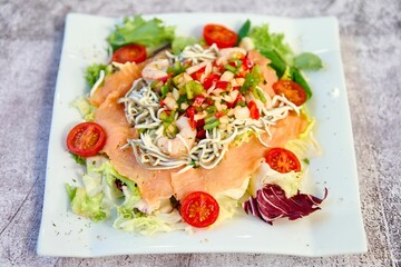White plate with a healthy, nutritious meal of fresh vegetables, fish and noodles