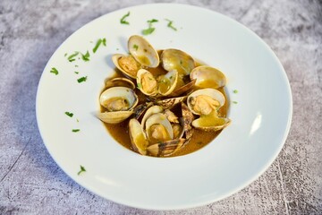 Plate of steamed clams served in a rich, aromatic brown sauce with a sprinkling of herbs for flavor