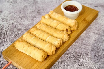 Spring rolls with sweet and sour sauce on a wooden board.