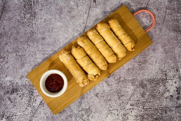 Spring rolls with sweet and sour sauce on a wooden board.