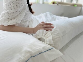 woman lying on a bed covered in pillows wearing a white shirt and blue trims