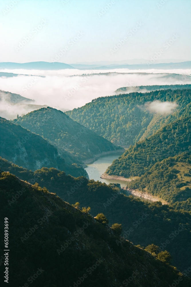 Poster a view of fog over some mountains with a river below