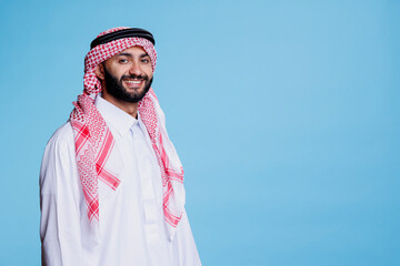 Cheerful muslim man with carefree expression dressed in traditional arabian clothes looking at camera. Smiling person wearing checkered red and white headdress studio portrait