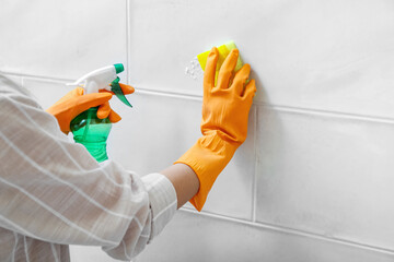 Woman in rubber gloves cleaning light tile with sponge, baking soda and sprayer