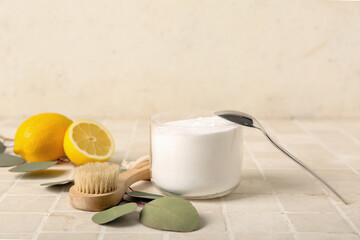 Bowl of baking soda, cleaning brush, lemons and eucalyptus branch on light tile table