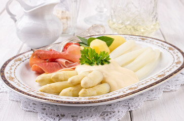 Traditional German white asparagus with serrano ham and boiled potatoes served as close-up on a...