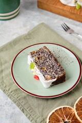 Sliced Polish poppy seed cake covered with white sugar glaze and garnished with candied fruits, on a green plate on a gray concrete background. Poppy baked goods.