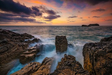 Scenic seascape at sunset with coastal rocks in the foreground.
