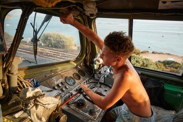 Caucasian man in the driver's cab of a large locomotive, adjusting a component over the window