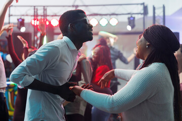 Carefree african american couple dancing together and having fun in nightclub. Cheerful young man and woman clubbers holding hands and partying on dancefloor while clubbing