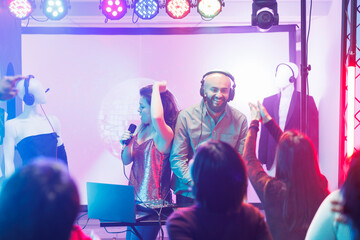 Dj and singer performing on stage while people dancing and enjoying show in nightclub. Diverse...