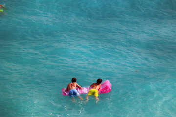 Młoda dziewczyna w stringach płynie na materacu po morzu.