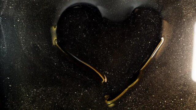 View from below through the glass on which honey is spilled. A woman is drawing a heart shape with her fingers on it, the concept of a love for honey.