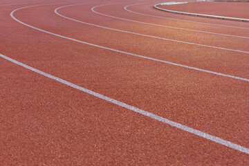 Fototapeta premium Close-up of the burgundy running track around the stadium illuminated by the morning light