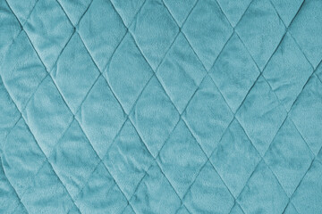 Quilted velours fabric background. Turquoise texture blanket or puffer jacket, stiched with diamond pattern, soft wrinkled surface, crupmed textile