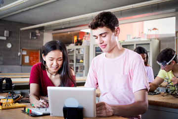 Multiracial boy and girl students at technical high school using a tablet in technology class. Classmates collaborating on a secondary school project: programming electric robots in laboratory.