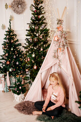 Child in christmas teepee surrounded by festive trees and warm holiday decor © Alena Vilgelm