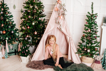 Girl sitting in cozy christmas tent with decorated trees and festive lights © Alena Vilgelm