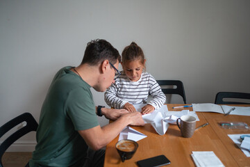 Father and child girl doing origami crafts together. Modern parenthood, weekend education...